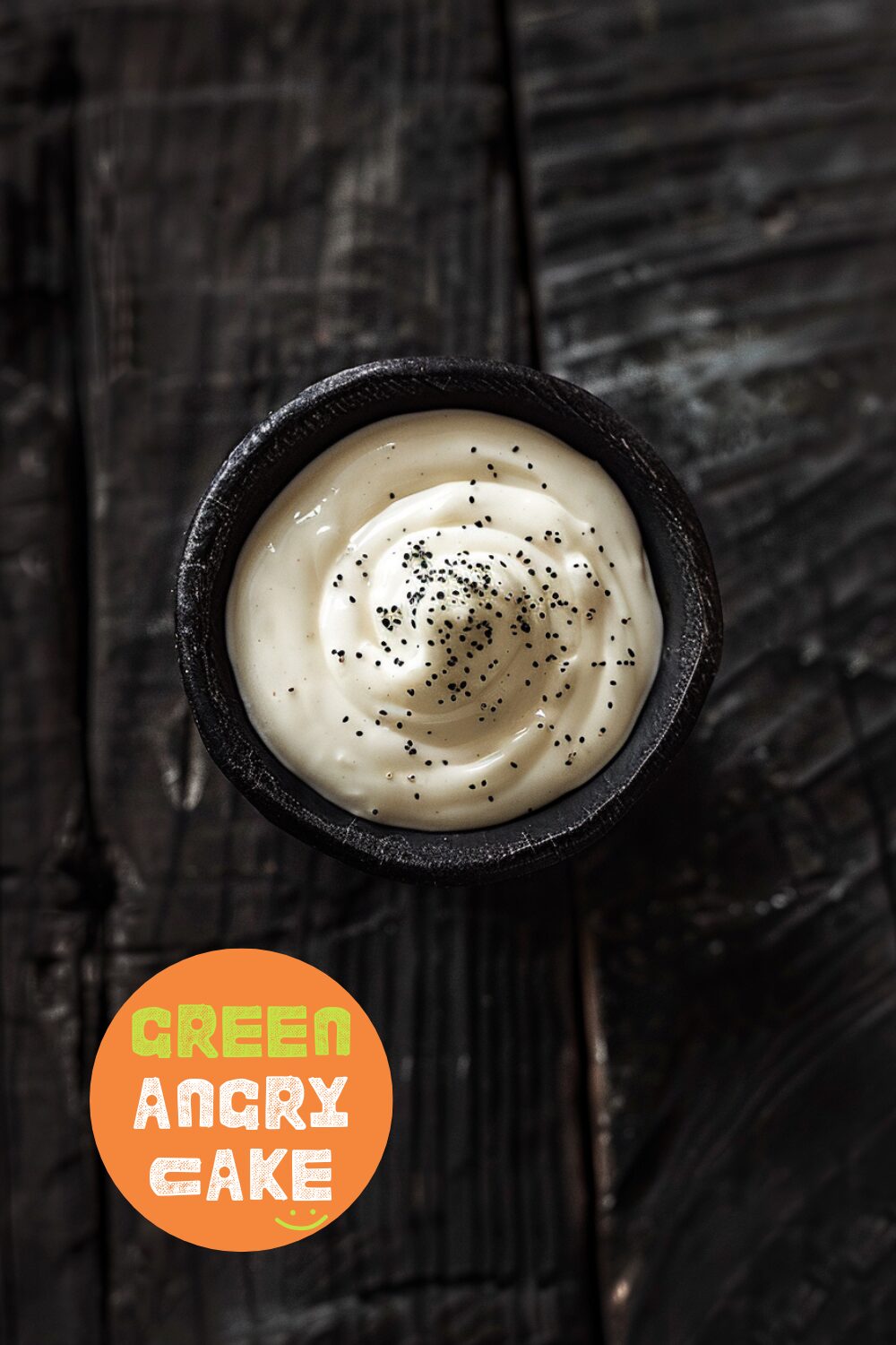 Top-down view of a bowl of creamy sour cream sauce on a dark, black wooden texture surface.