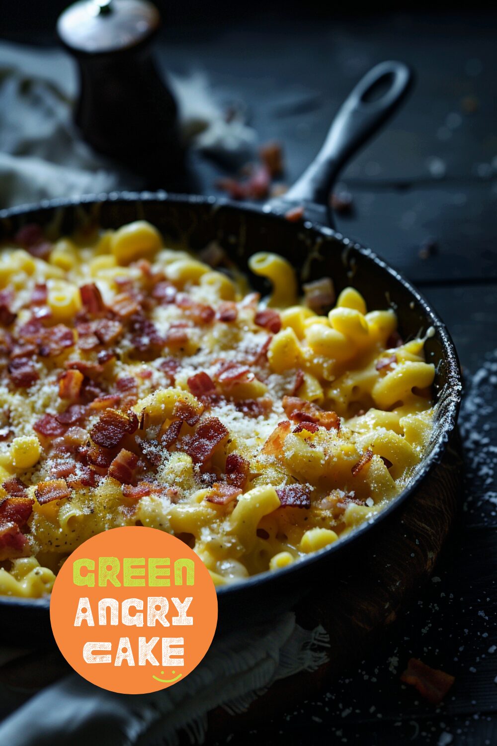 Close-up side view of mac & cheese being prepared in a skillet, with bacon bits being added to the cheesy pasta on a dark wooden surface.