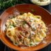 Top-down view of a creamy chicken Alfredo dish on a white plate, set against a dark, black wooden texture surface.