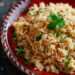 A top-down view of a bowl of Mexican rice on a red plate, displayed on a dark, black wooden texture surface.