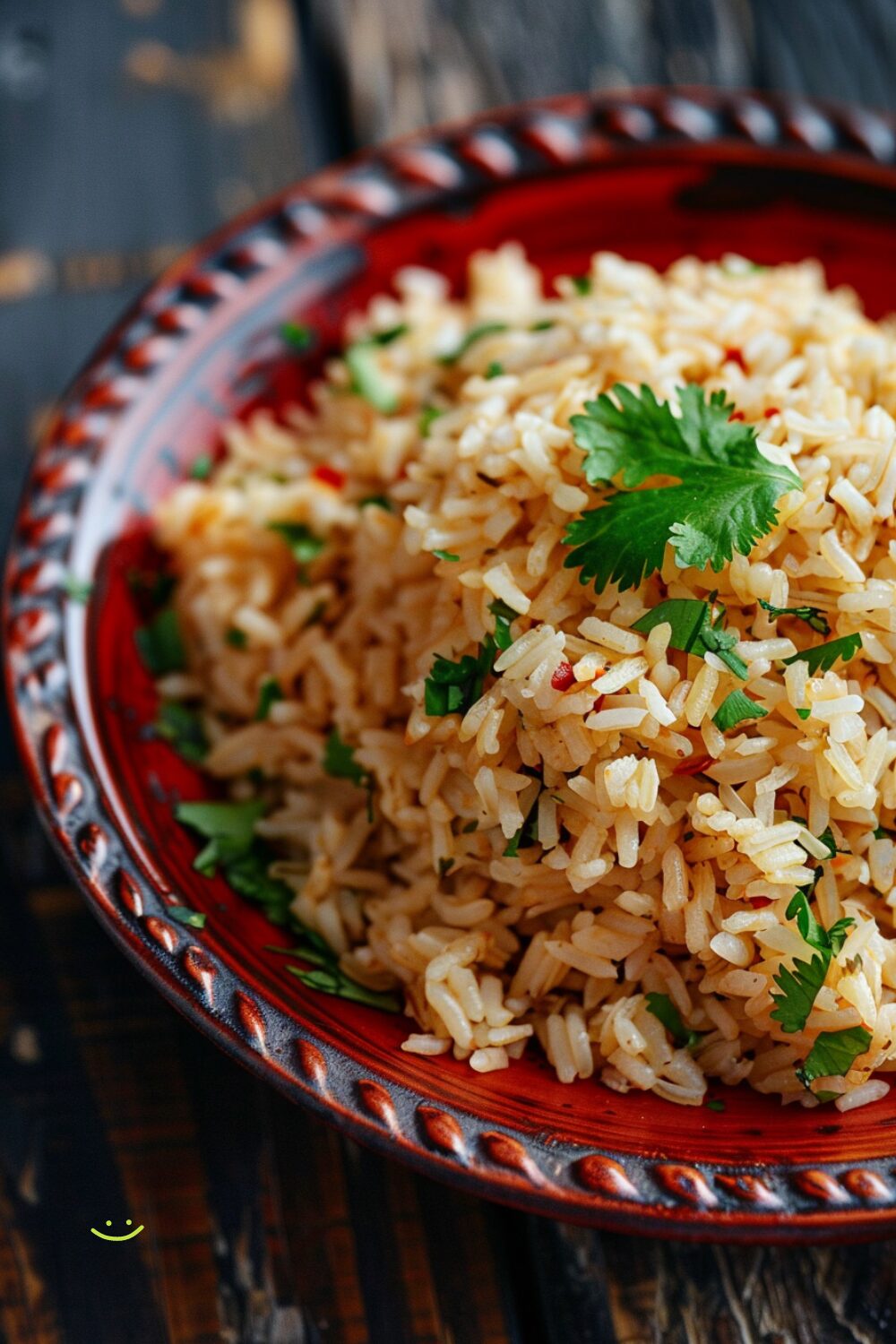 A top-down view of a bowl of Mexican rice on a red plate, displayed on a dark, black wooden texture surface.