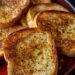 Top-down view of perfectly crispy Texas toast on a blue plate, set against a dark, black wooden background.