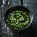 Top-down view of a bowl of green chile sauce on a dark, black wooden texture surface.