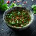 Top-down view of a bowl of Nước Chấm on a dark, black wooden texture surface.