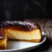 Top-down view of a Basque cheesecake with a deeply caramelized top on a white plate, set on a dark wooden surface