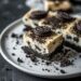 Top-down view of Oreo cheesecake bars on a white plate, set on a dark wooden surface