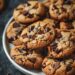 Top-down view of brown butter chocolate chip cookies on a white plate, set on a dark wooden surface