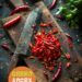 A vibrant photo showing freshly chopped chillies on a chopping board, with a sharp knife nearby. The background is a dark, black wooden texture surface. This image demonstrates chilli preparation techniques.